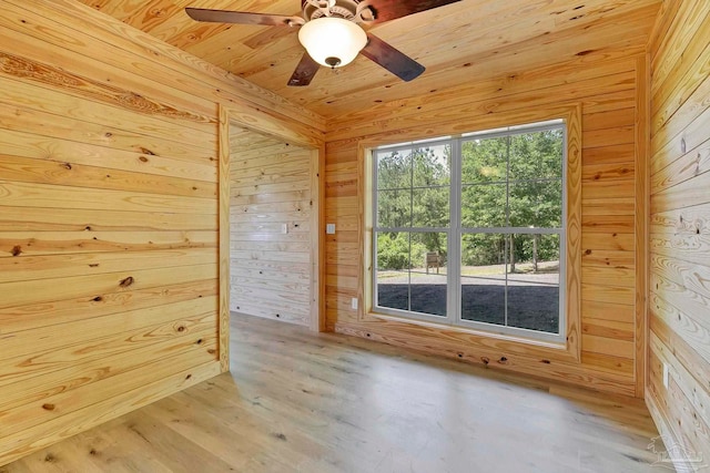 empty room featuring wooden walls, wooden ceiling, ceiling fan, and light wood-style flooring