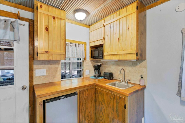 kitchen featuring light brown cabinetry, black microwave, a sink, backsplash, and refrigerator