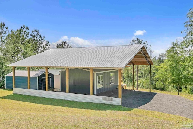 rear view of property featuring a shed, a lawn, an outdoor structure, driveway, and metal roof
