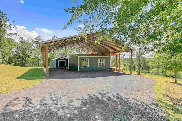 view of front facade featuring a storage shed, a carport, an outdoor structure, gravel driveway, and a front lawn
