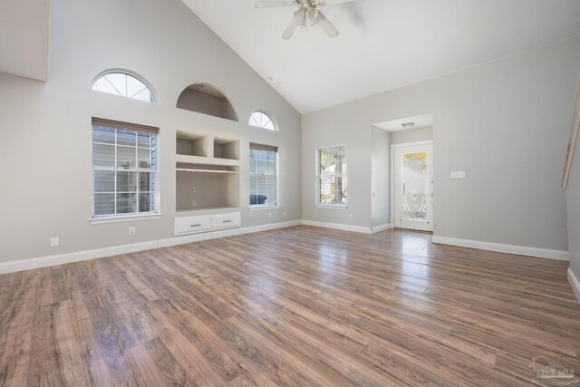 unfurnished living room with ceiling fan, wood-type flooring, built in features, and high vaulted ceiling