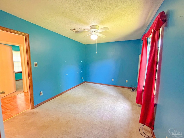 carpeted empty room with baseboards, visible vents, a ceiling fan, and a textured ceiling