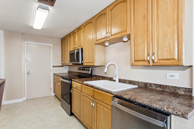 kitchen with appliances with stainless steel finishes, dark stone countertops, and sink