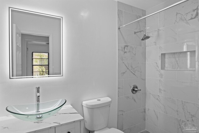 bathroom with tiled shower, toilet, and vanity