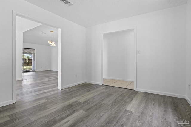 empty room with visible vents, baseboards, a notable chandelier, and wood finished floors