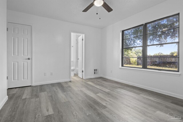 unfurnished bedroom featuring visible vents, baseboards, wood finished floors, ensuite bath, and a textured ceiling