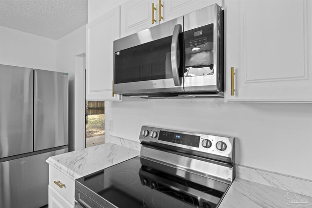 kitchen featuring light stone counters, stainless steel appliances, a textured ceiling, white cabinetry, and marble finish floor