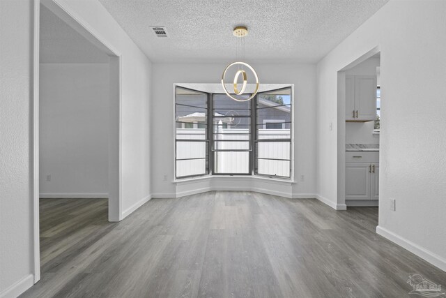 unfurnished dining area featuring visible vents, a textured ceiling, wood finished floors, an inviting chandelier, and baseboards