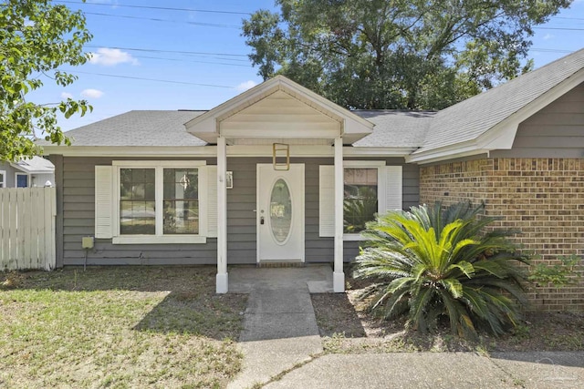 property entrance featuring brick siding, roof with shingles, and fence