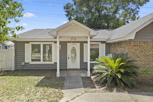 view of exterior entry featuring fence, brick siding, and roof with shingles