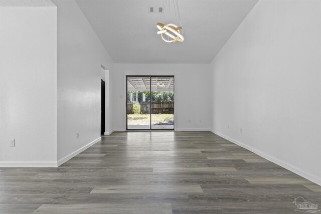 spare room featuring visible vents, baseboards, a chandelier, lofted ceiling, and wood finished floors