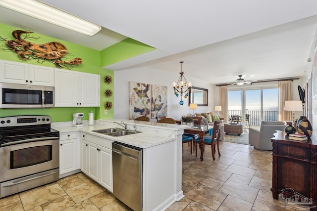 kitchen with kitchen peninsula, ceiling fan with notable chandelier, stainless steel appliances, sink, and white cabinetry