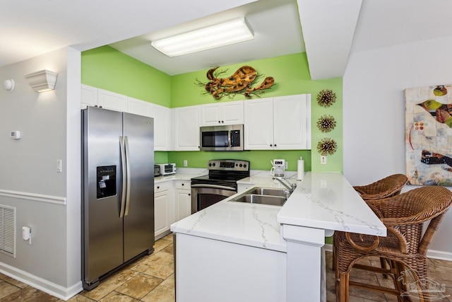 kitchen with kitchen peninsula, a kitchen bar, stainless steel appliances, sink, and white cabinetry