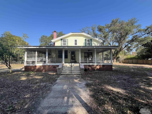 country-style home featuring fence, covered porch, a chimney, and a sunroom