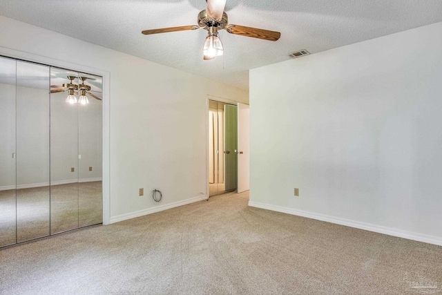 unfurnished bedroom featuring light carpet, ceiling fan, multiple closets, and a textured ceiling