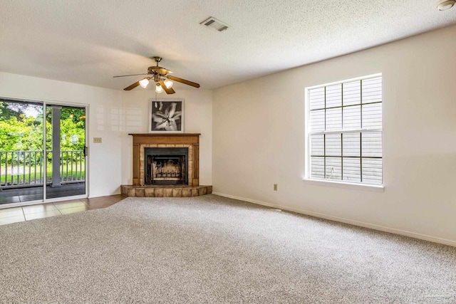 unfurnished living room featuring a textured ceiling, a tiled fireplace, carpet flooring, and ceiling fan