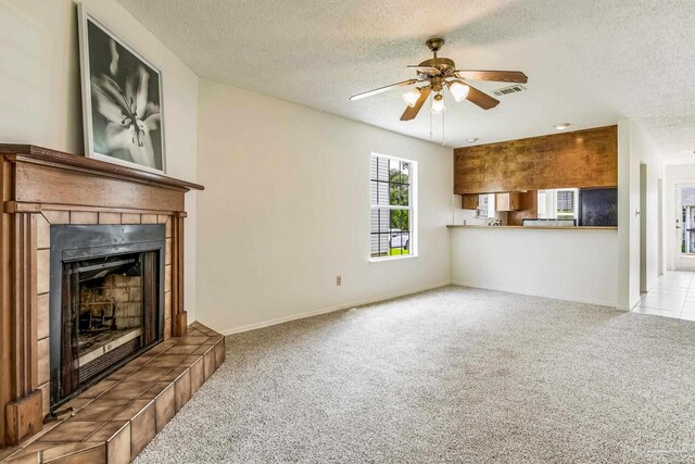 unfurnished living room featuring light carpet, a tiled fireplace, and a textured ceiling