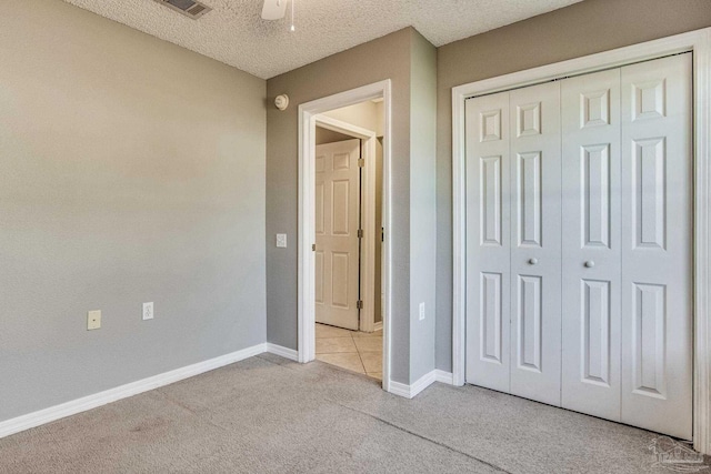 unfurnished bedroom featuring a closet, a textured ceiling, light colored carpet, and ceiling fan