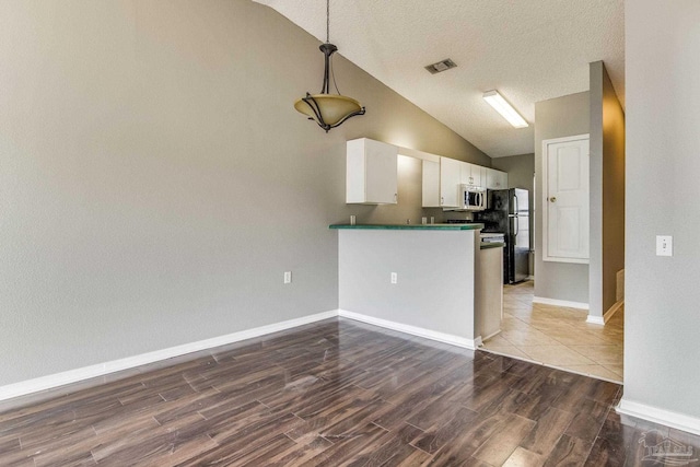 kitchen with hardwood / wood-style flooring, black refrigerator, kitchen peninsula, vaulted ceiling, and white cabinets