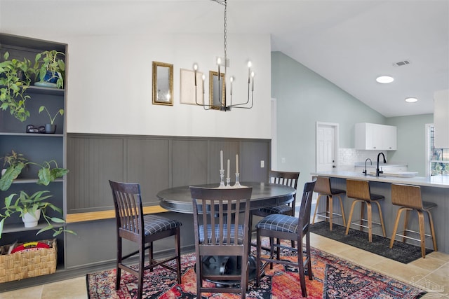 dining area featuring vaulted ceiling, wainscoting, tile patterned floors, and an inviting chandelier