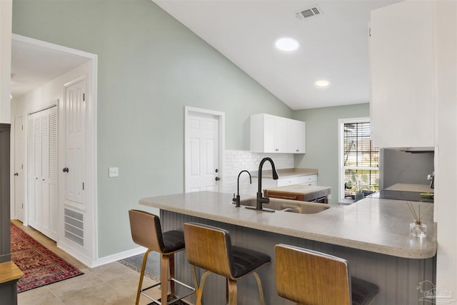 kitchen featuring visible vents, a breakfast bar, vaulted ceiling, white cabinetry, and a sink