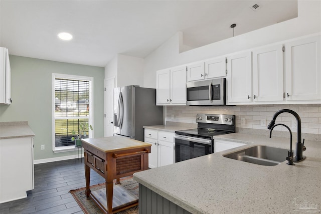 kitchen with appliances with stainless steel finishes, a sink, white cabinetry, and tasteful backsplash