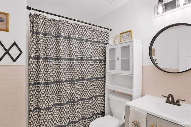 full bath featuring toilet, a shower with curtain, a wainscoted wall, and vanity