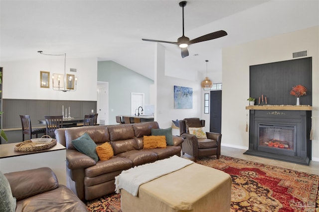 living area featuring ceiling fan with notable chandelier, visible vents, a glass covered fireplace, vaulted ceiling, and tile patterned floors