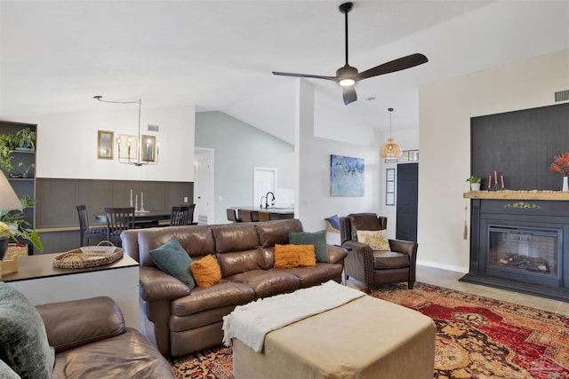 tiled living area featuring high vaulted ceiling, visible vents, ceiling fan with notable chandelier, and a glass covered fireplace