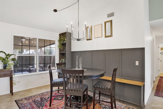 tiled dining area with a wainscoted wall, a notable chandelier, and visible vents