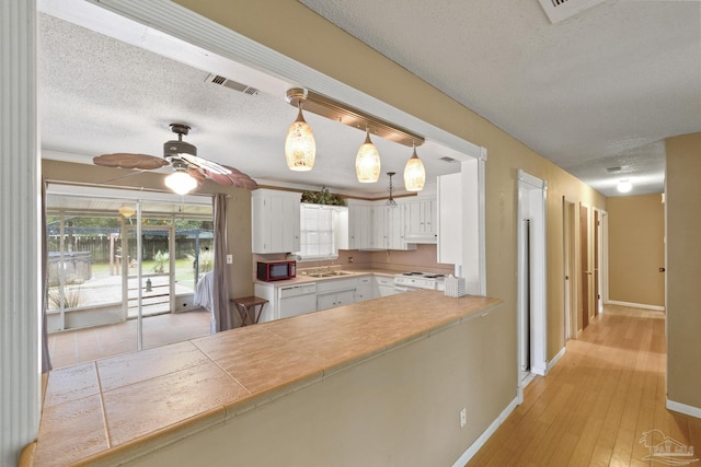 kitchen featuring white appliances, white cabinets, hanging light fixtures, and a textured ceiling