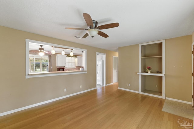 spare room featuring ceiling fan, light wood-type flooring, built in features, and a textured ceiling