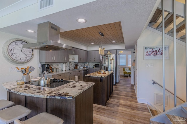 kitchen featuring dark brown cabinetry, visible vents, stainless steel fridge with ice dispenser, island exhaust hood, and black electric stovetop