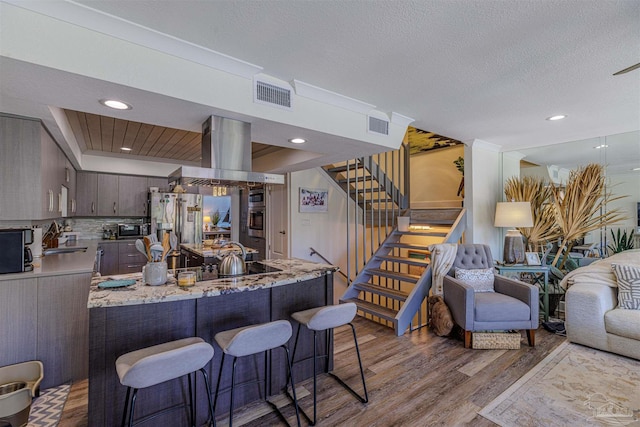 kitchen featuring visible vents, appliances with stainless steel finishes, open floor plan, island exhaust hood, and a sink