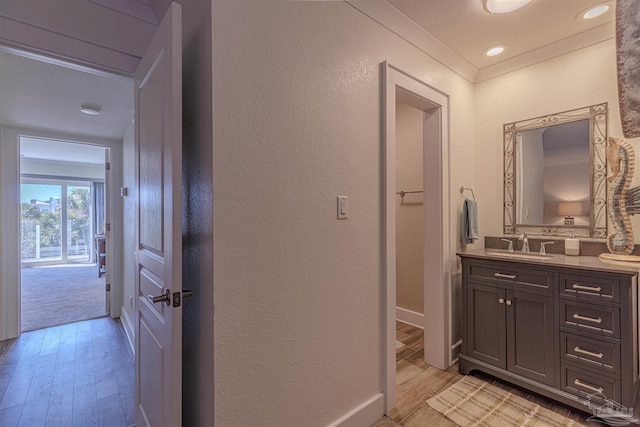 bathroom featuring a textured wall, ornamental molding, vanity, wood finished floors, and baseboards