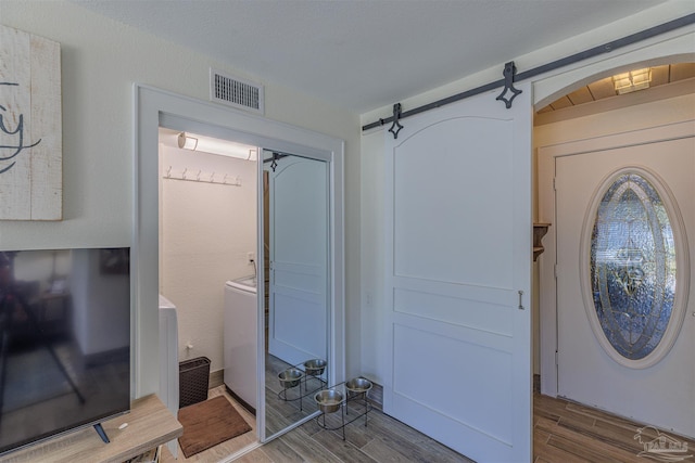 interior space with a barn door, washer and clothes dryer, wood finished floors, and visible vents