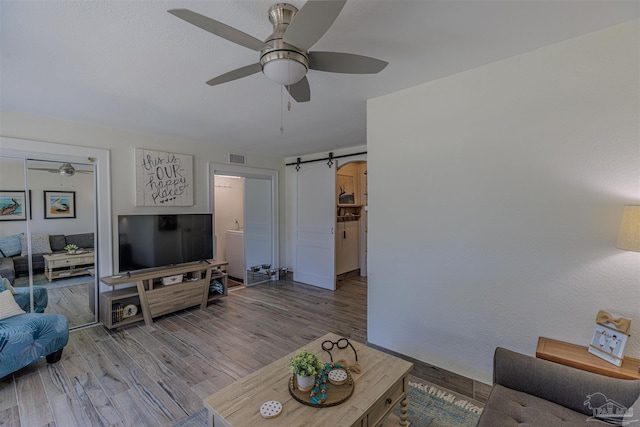 living room featuring a barn door, visible vents, ceiling fan, and wood finished floors