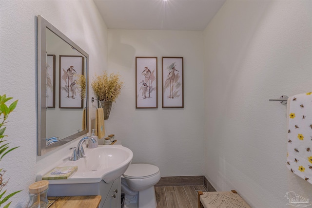 bathroom featuring toilet, baseboards, wood finished floors, and vanity