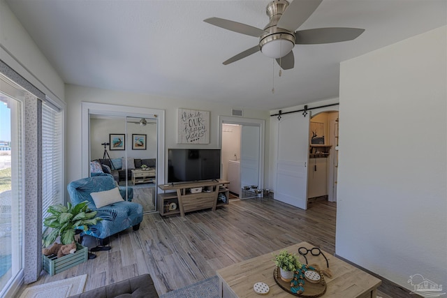 living room featuring wood finished floors, visible vents, ceiling fan, and a barn door