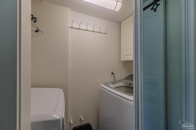 laundry area with cabinet space and a textured wall