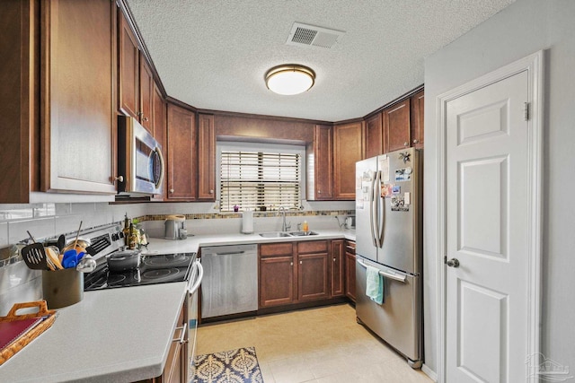 kitchen with appliances with stainless steel finishes, sink, a textured ceiling, and decorative backsplash