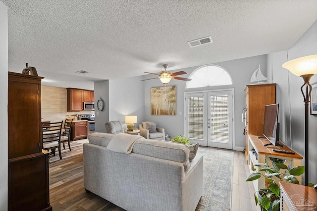 living room with dark wood-type flooring, ceiling fan, french doors, and a textured ceiling