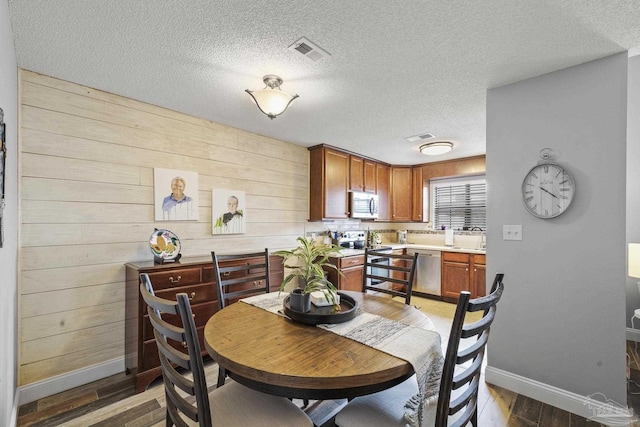 dining area with sink, wooden walls, dark hardwood / wood-style floors, and a textured ceiling