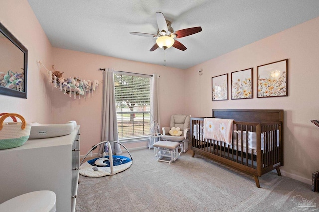 carpeted bedroom with ceiling fan, a nursery area, and a textured ceiling