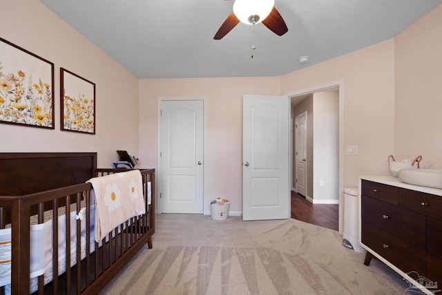 carpeted bedroom featuring ceiling fan, sink, and a nursery area