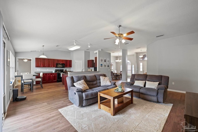 living room featuring ceiling fan with notable chandelier, vaulted ceiling, and light hardwood / wood-style flooring