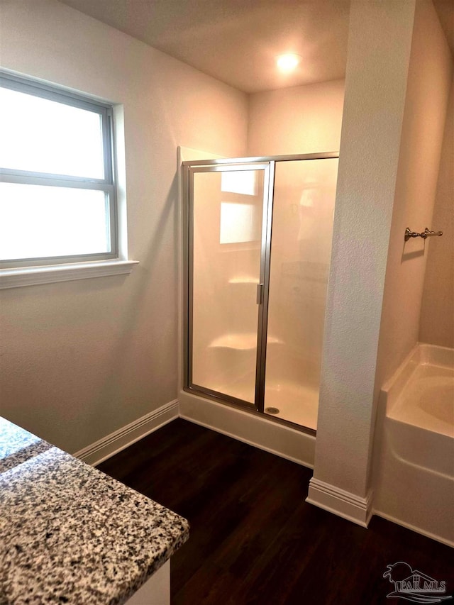 bathroom featuring a stall shower, baseboards, a garden tub, and wood finished floors