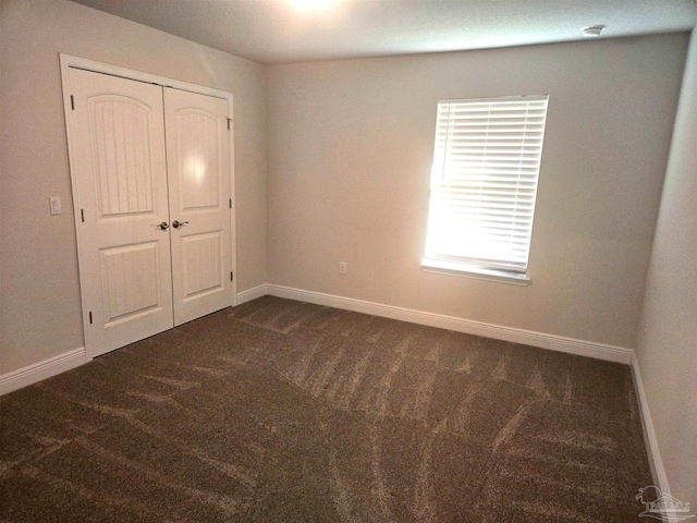 unfurnished bedroom with a closet, dark carpet, and baseboards