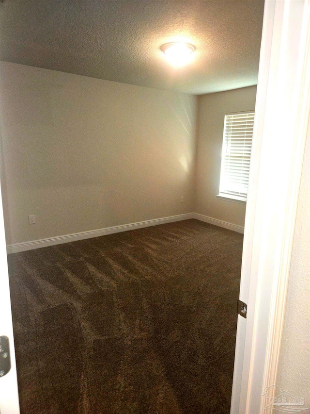 empty room with a textured ceiling, dark colored carpet, and baseboards