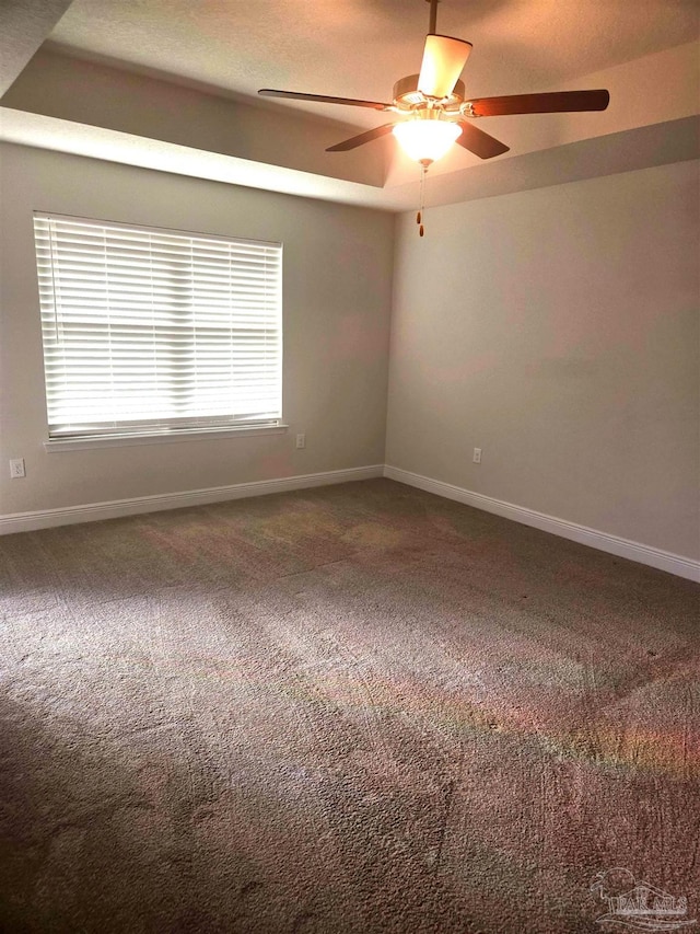 carpeted spare room with a ceiling fan and baseboards